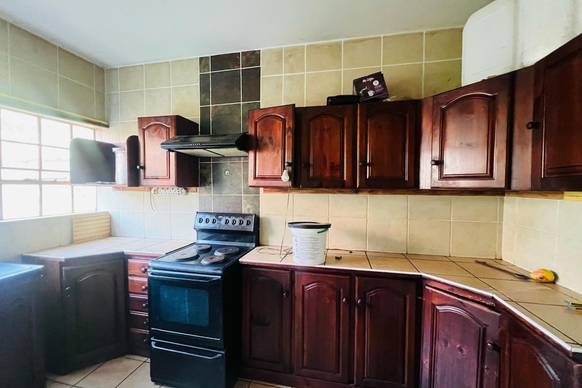 A dated kitchen featuring dark wood cabinetry, tiled countertops, and a freestanding electric stove with an extractor fan.