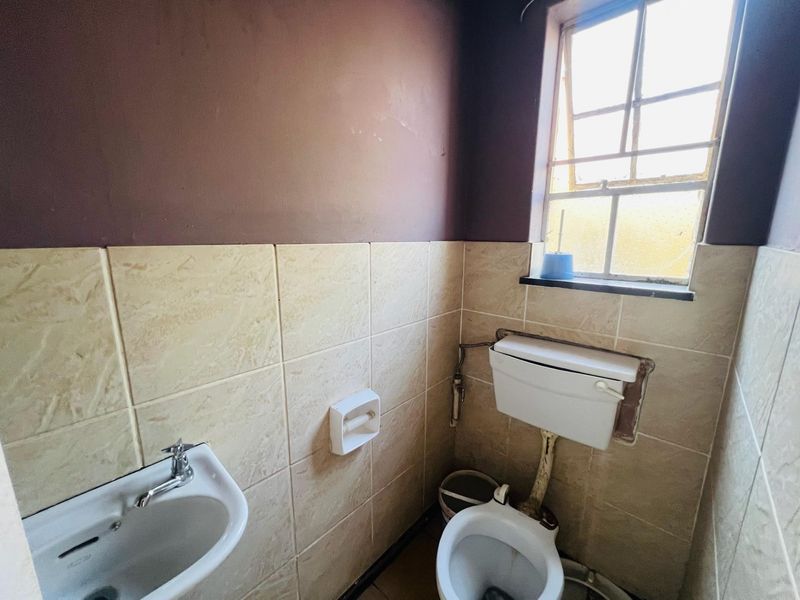 A compact bathroom featuring a pedestal washbasin, toilet with cistern, and partial wall tiling. The space requires cosmetic updates to improve its condition.