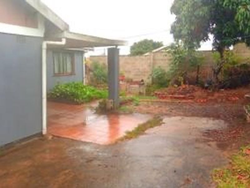 Rear exterior view of the property featuring a covered tiled patio, concrete boundary wall, and an unlandscaped garden area with drainage issues.