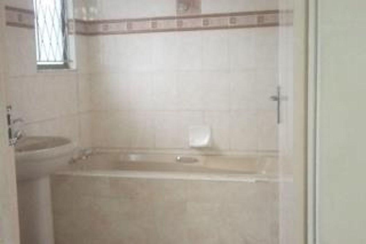 A dated bathroom featuring a pedestal basin and a built-in bathtub with tiled walls and security bars on the window.