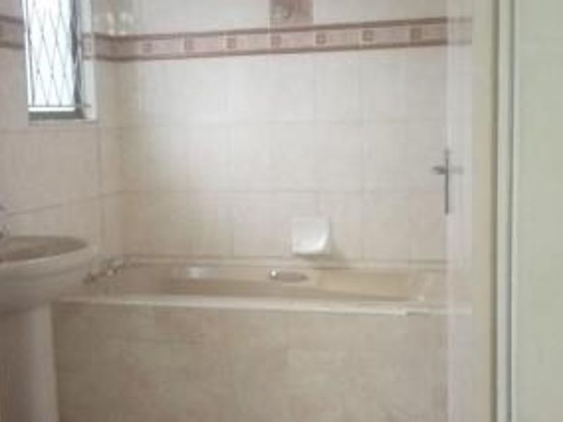 A dated bathroom featuring a pedestal basin and a built-in bathtub with tiled walls and security bars on the window.