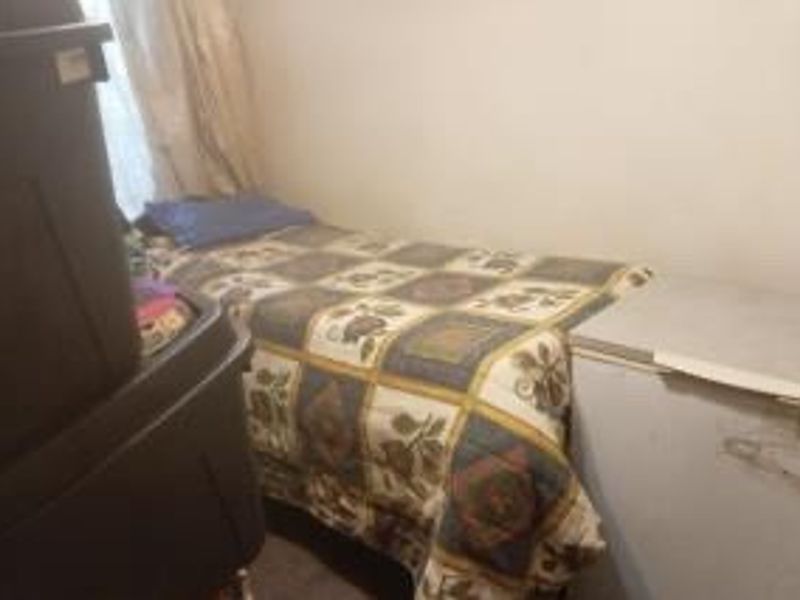 A small bedroom space with basic finishes, currently used for storage and sleeping.