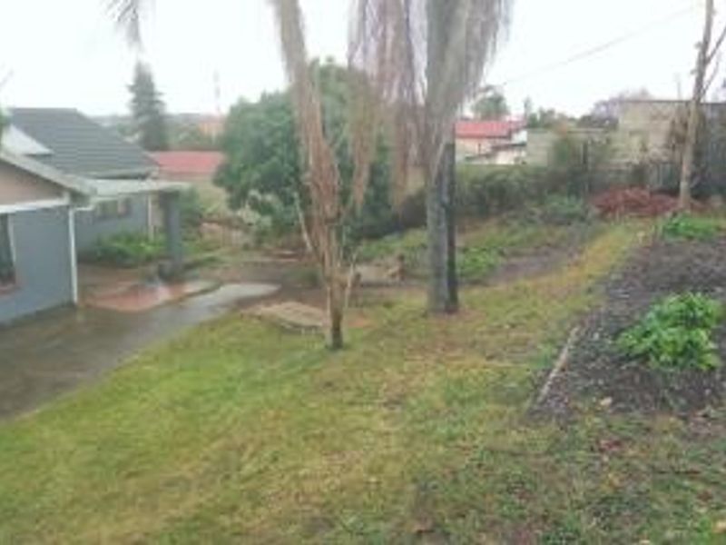 A view of the rear exterior of the house featuring a paved patio area, a tiled roof, and a large, sloped garden space.