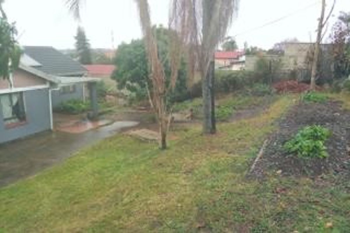 A view of the rear exterior of the house featuring a paved patio area, a tiled roof, and a large, sloped garden space.