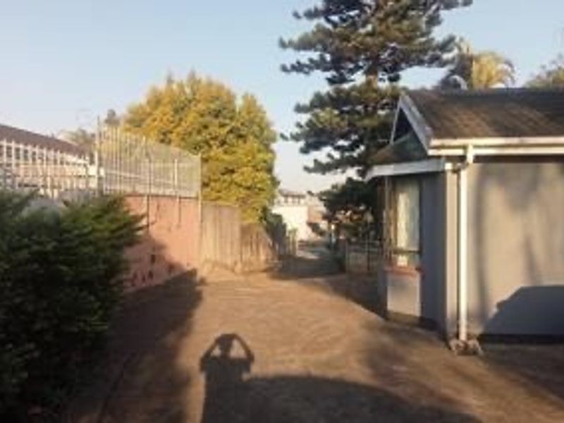 A view of the property's paved driveway and side elevation, featuring perimeter fencing and established trees.