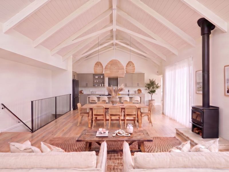 Spacious open-plan living and dining area featuring a vaulted ceiling with exposed beams, hardwood floors, and a modern freestanding wood-burning fireplace.
