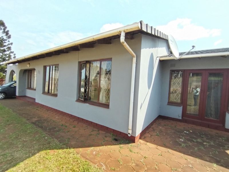 Rear exterior view of the house featuring a paved patio area, security-barred windows, and functional guttering system.
