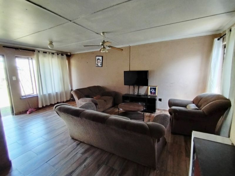 A living room featuring tiled flooring, a ceiling fan, and security bars on the windows, offering a functional space with potential for cosmetic updates.