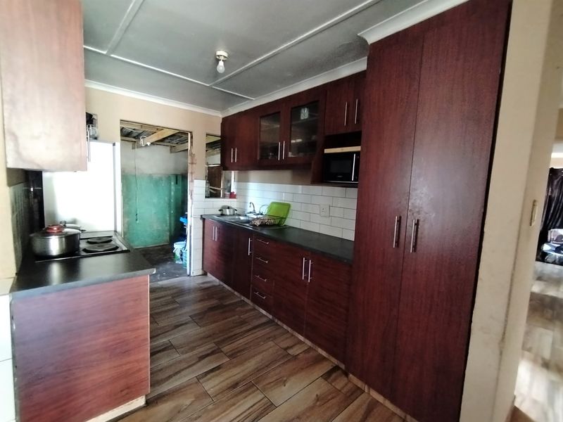 A functional kitchen featuring dark wood-finish cabinetry, a subway tile backsplash, and an electric hob, with an adjacent unfinished utility area.