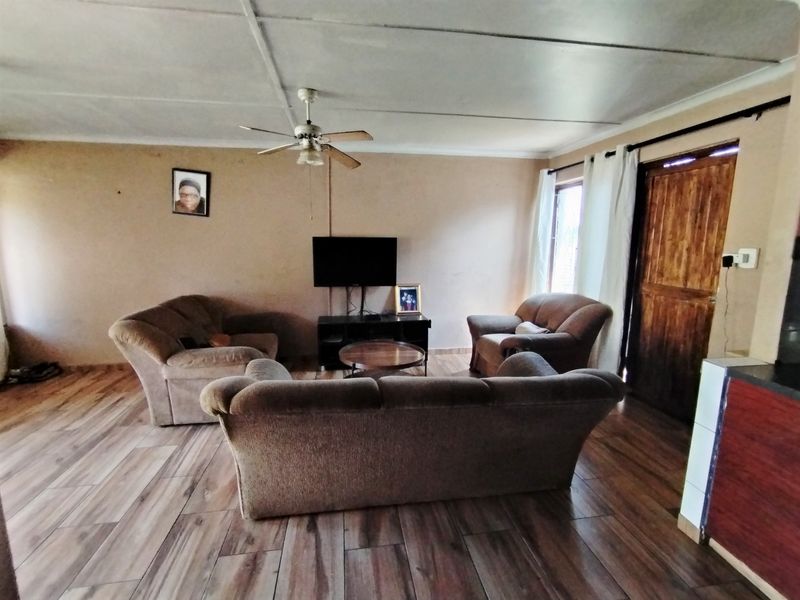 A living room featuring laminate flooring, a ceiling fan, and a wooden entrance door, offering a functional space with potential for cosmetic updates.