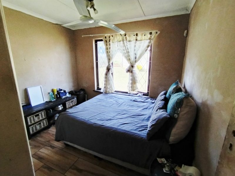 A bedroom featuring tiled flooring, a ceiling fan, and a leaded glass window. The walls require cosmetic attention and refinishing.