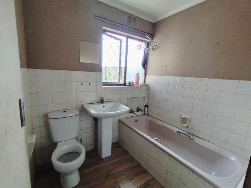 A dated bathroom featuring a pedestal basin, toilet, and bathtub with tiled splashbacks, requiring cosmetic updates to improve its overall condition and appeal.