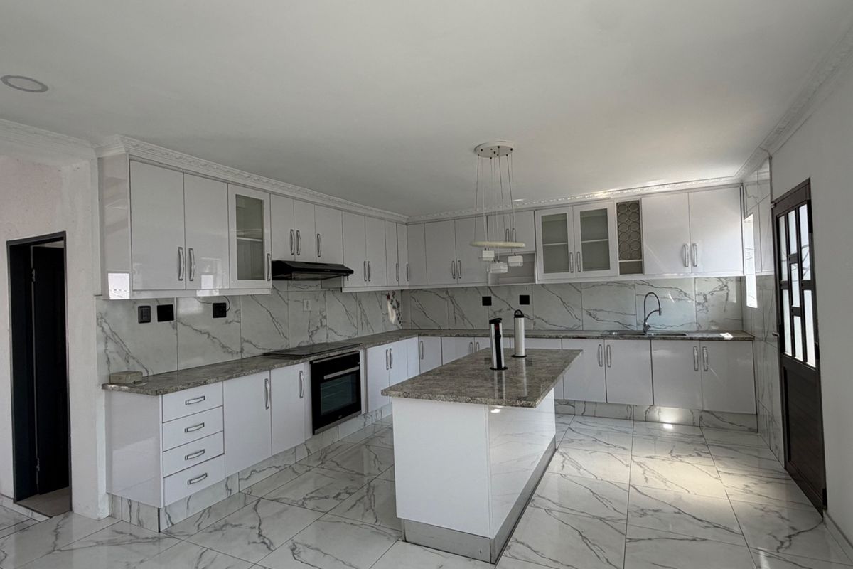 A modern, spacious kitchen featuring white cabinetry, granite countertops, a central island, and marble-effect tiled flooring and backsplash.