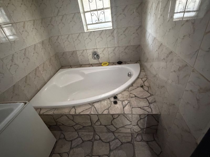 A bathroom featuring a corner bathtub with stone-effect tiled surround and wall tiling, requiring minor repairs to fixtures and finishes.