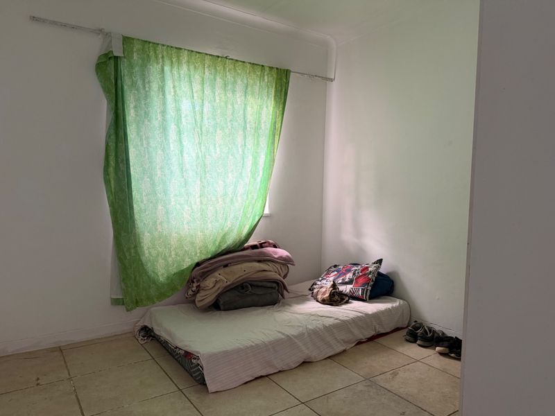 A basic bedroom featuring tiled flooring and a window with a curtain rail, requiring cosmetic updates and repairs to finishes.