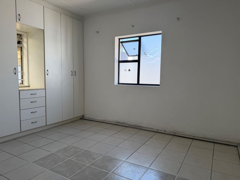 An empty bedroom featuring white built-in cupboards, tiled flooring, and a single window with an aluminium frame.