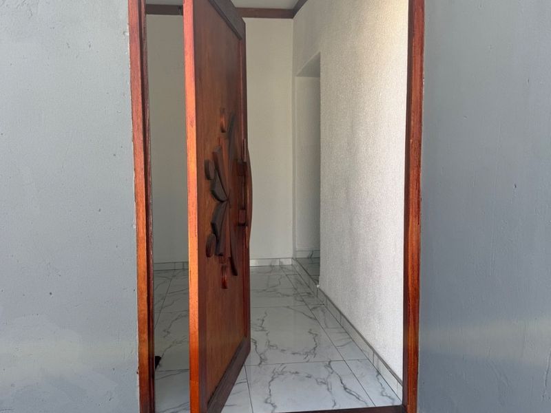 A modern entrance featuring a decorative solid wood pivot door and marble-look tiled flooring, providing a clean and welcoming transition into the home.