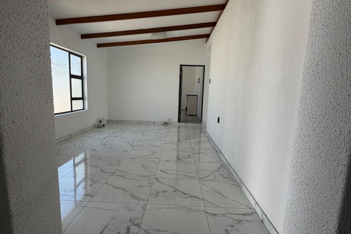 A bright, empty living area featuring modern marble-look floor tiles, exposed timber ceiling beams, and textured walls, offering a clean canvas for interior design.