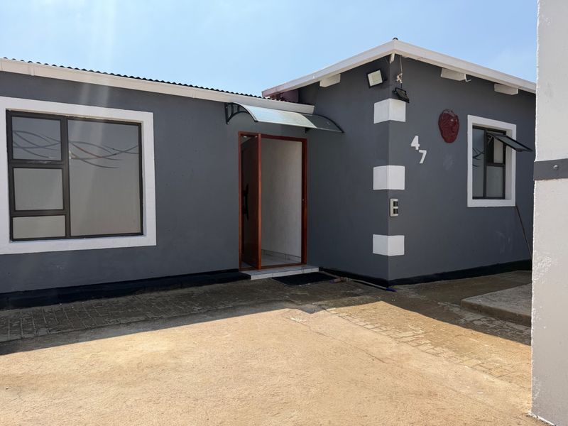 Front elevation of a residential property featuring a paved driveway, grey exterior walls with white accents, and aluminium window frames.