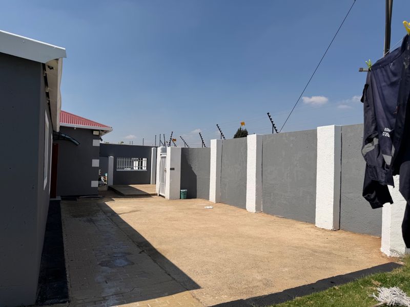 A paved rear courtyard area enclosed by a high perimeter wall with electric fencing, providing a secure and private outdoor space.