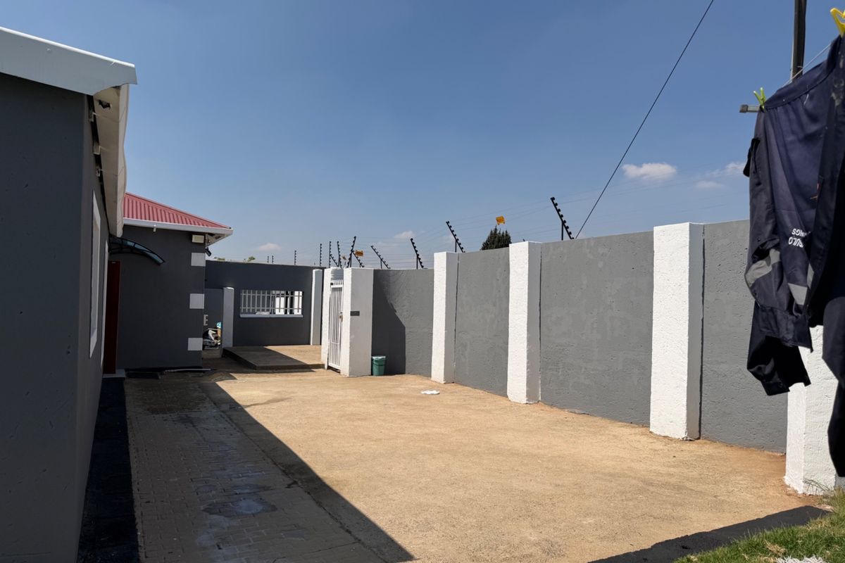 A paved rear courtyard area enclosed by a high perimeter wall with electric fencing, providing a secure and private outdoor space.