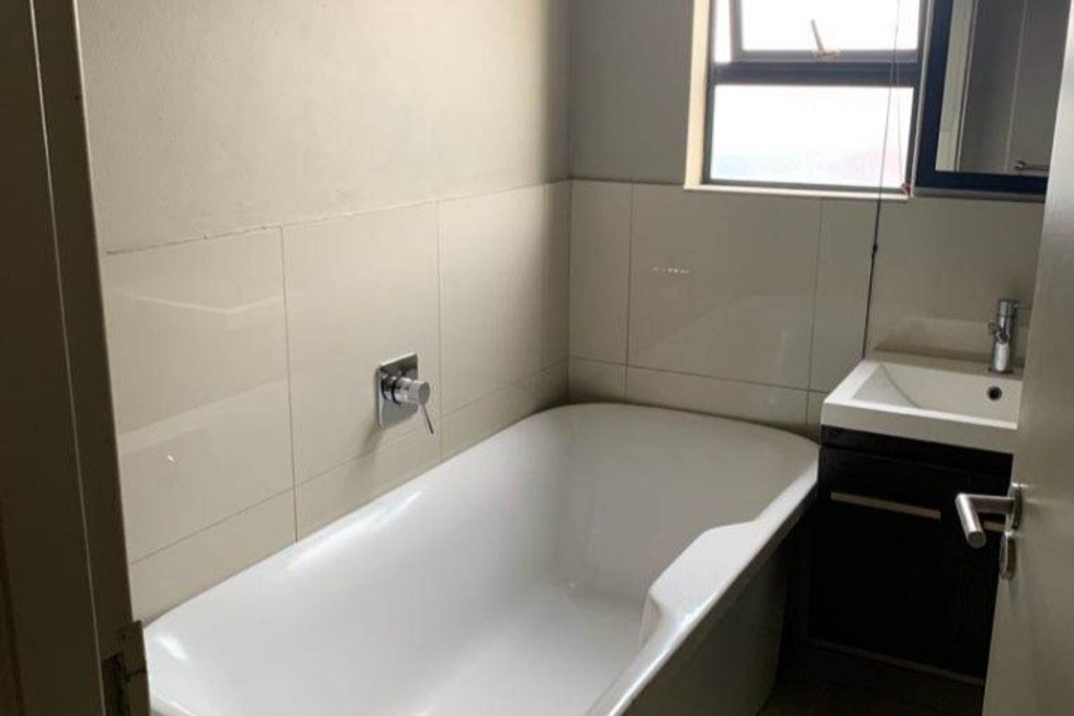 A clean and functional bathroom featuring a modern freestanding bathtub, vanity cabinet with basin, and neutral wall tiling.