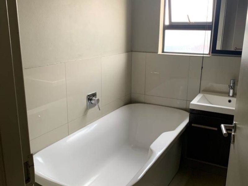 A clean and functional bathroom featuring a modern freestanding bathtub, vanity cabinet with basin, and neutral wall tiling.