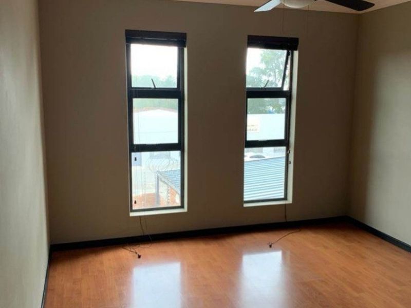 A bright, empty bedroom featuring laminate flooring, a ceiling fan, and dual windows with aluminium frames.