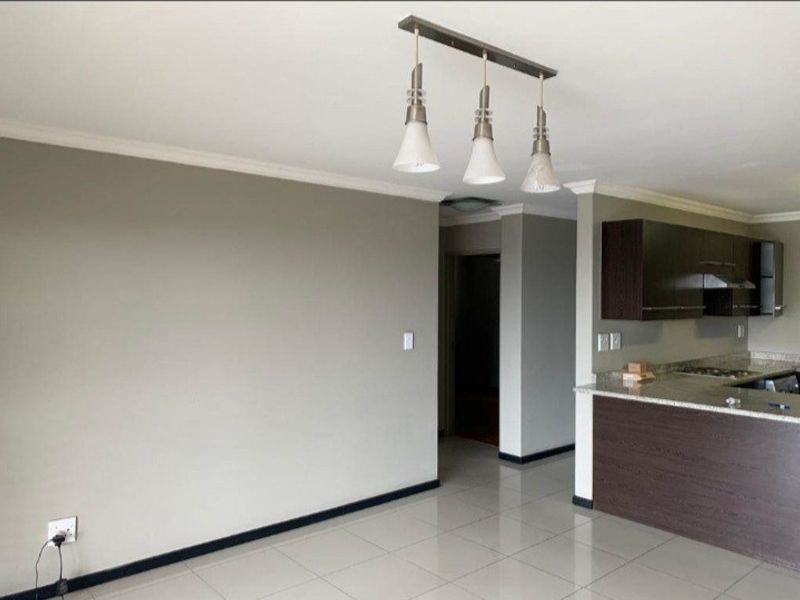 An open-plan living and kitchen area featuring modern dark cabinetry, granite countertops, integrated hob, and neutral tiled flooring throughout.