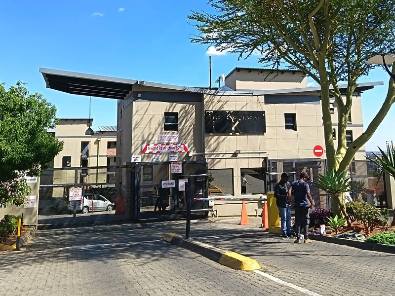 The main entrance and security gatehouse of the apartment complex, featuring controlled access, paved driveway, and modern architectural facade.