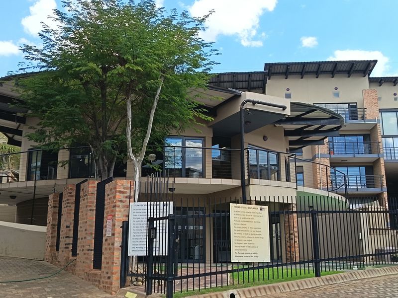 Exterior view of a modern apartment complex featuring brick boundary walls, metal security fencing, and multi-level balconies with sliding glass doors.