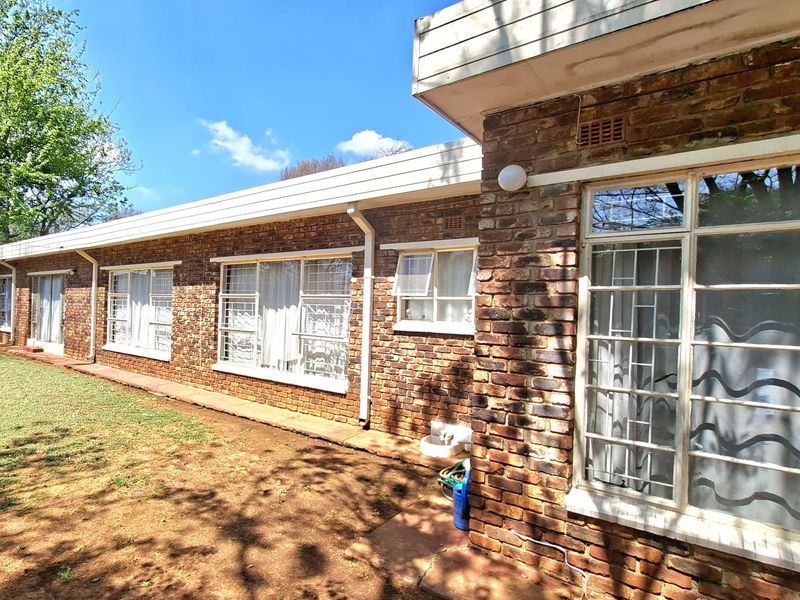 Rear exterior view of the house featuring a classic face brick facade, steel-framed windows with security bars, and established garden space.