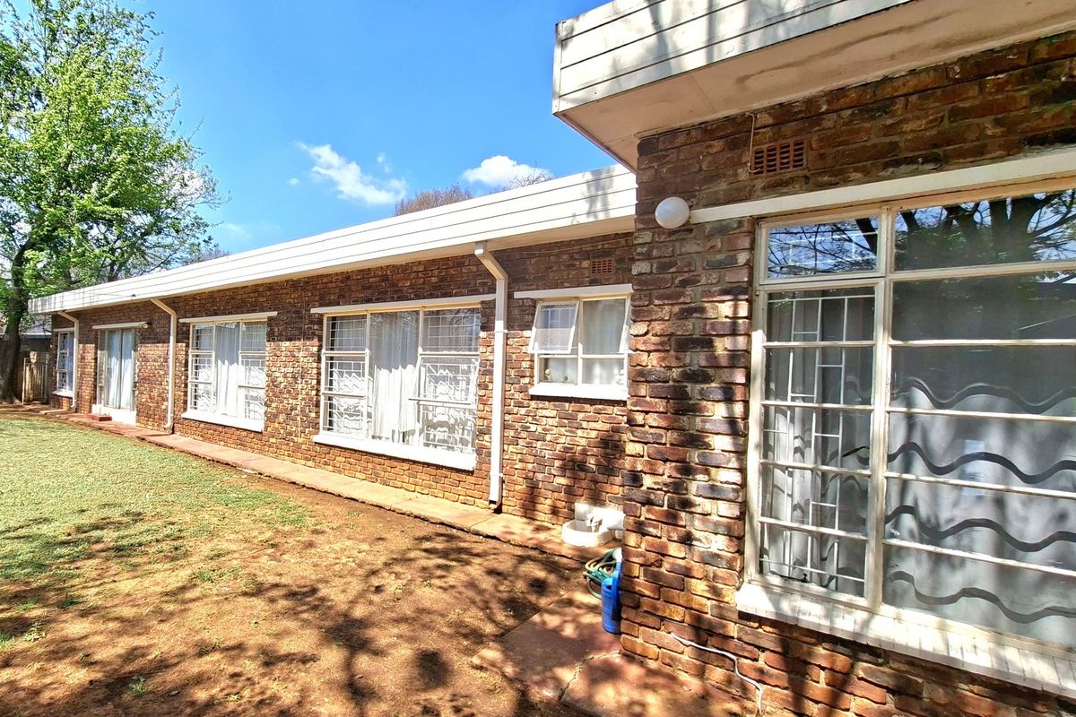 Rear exterior view of the house featuring a classic face brick facade, steel-framed windows with security bars, and established garden space.