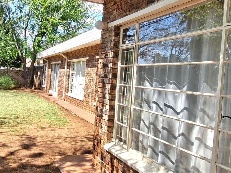 Rear exterior view of the house featuring face brick walls, steel-framed windows, and a concrete patio area overlooking the garden.