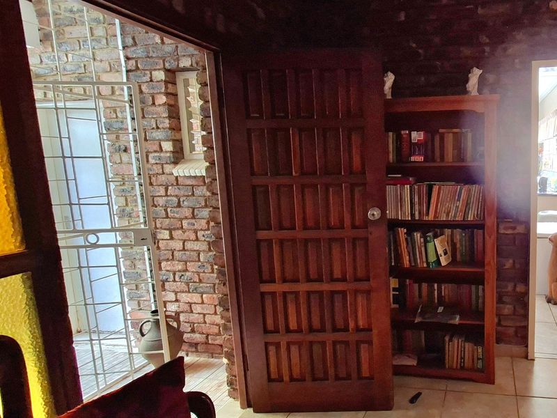 A hallway featuring exposed brick walls, tiled flooring, and a solid timber panel door leading to an outdoor area with a security gate.