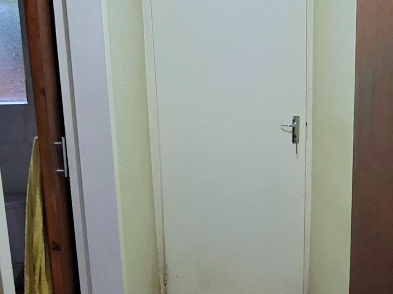 A narrow hallway featuring tiled flooring and a white internal door, showing signs of wear on the walls and door frame.