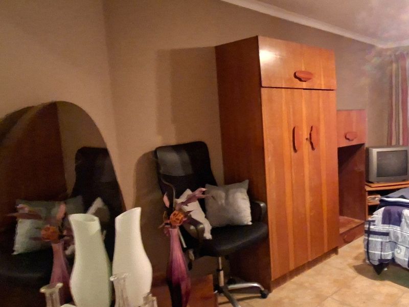 A bedroom featuring tiled flooring and a built-in wooden wardrobe, offering a functional space with neutral wall tones.