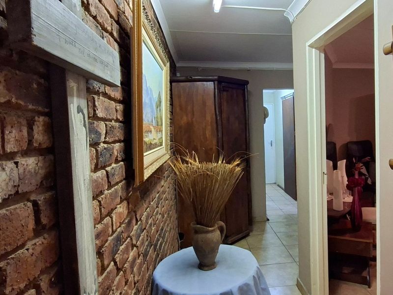 A hallway featuring an exposed brick feature wall, tiled flooring, and coved ceilings, providing access to adjacent rooms.