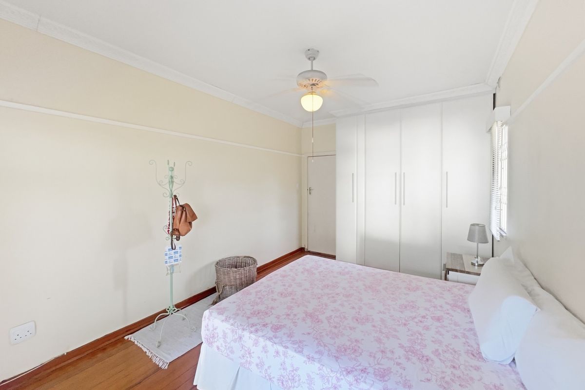 A well-maintained bedroom featuring polished timber flooring, built-in white cabinetry, and a ceiling fan, offering a clean and functional living space.