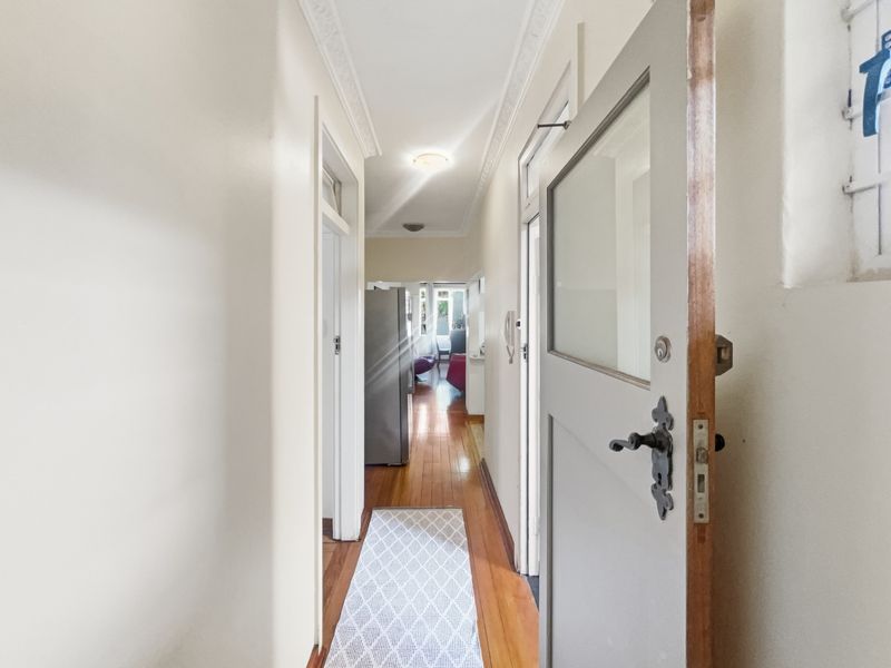 A bright hallway featuring polished hardwood flooring and ornate ceiling cornicing, providing access to adjacent rooms within the apartment.