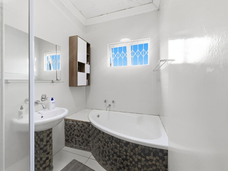 A functional bathroom featuring a corner bathtub, pedestal basin, and wall-mounted storage, finished with distinctive pebble-style tiling.