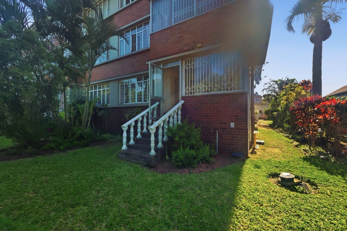 Rear view of a brick apartment building featuring a garden area and a concrete staircase leading to the entrance.
