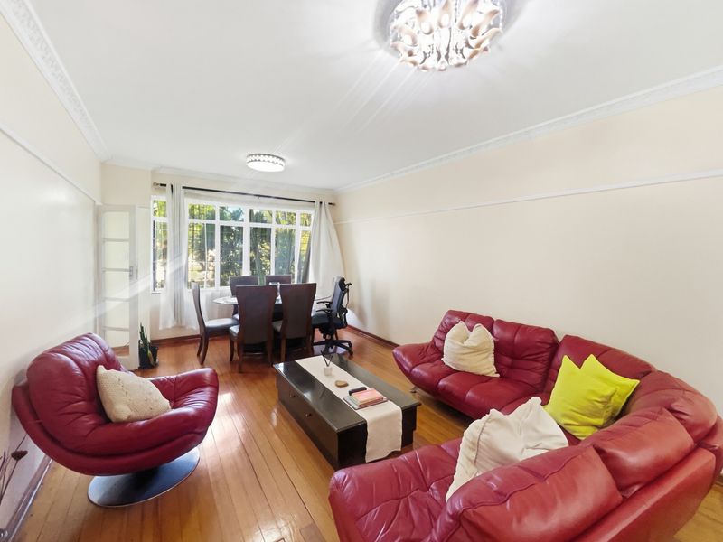 Spacious open-plan living and dining area featuring polished hardwood flooring, decorative crown molding, and large windows providing ample natural light.
