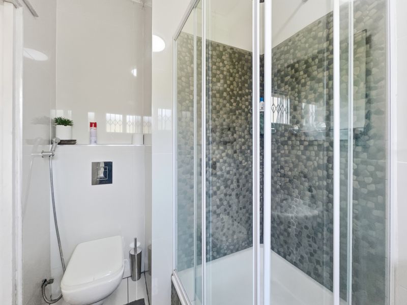 A modern bathroom featuring a wall-mounted toilet with a concealed cistern and a glass-enclosed shower with decorative pebble-style mosaic wall tiling.