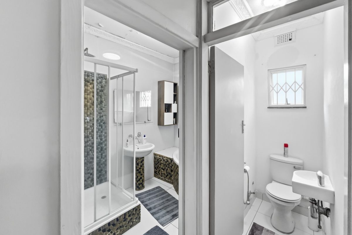 A functional bathroom featuring a shower enclosure with pebble tile accents, a pedestal basin, and a separate toilet area with a small wall-mounted sink.