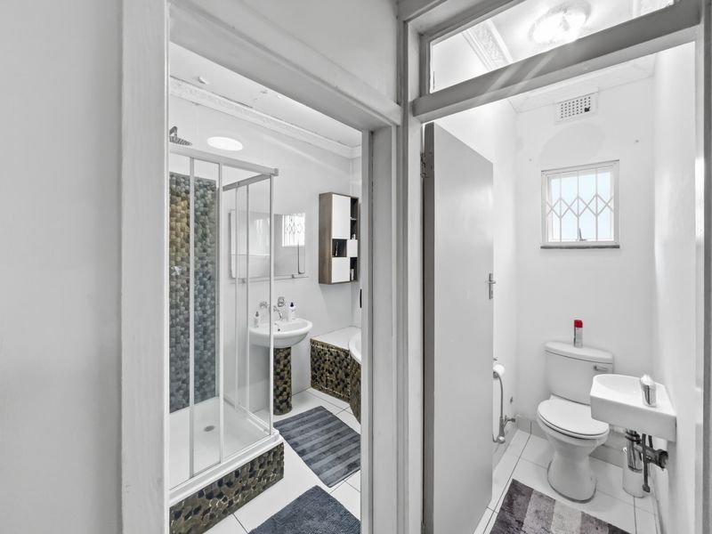 A functional bathroom featuring a shower enclosure with pebble tile accents, a pedestal basin, and a separate toilet area with a small wall-mounted sink.