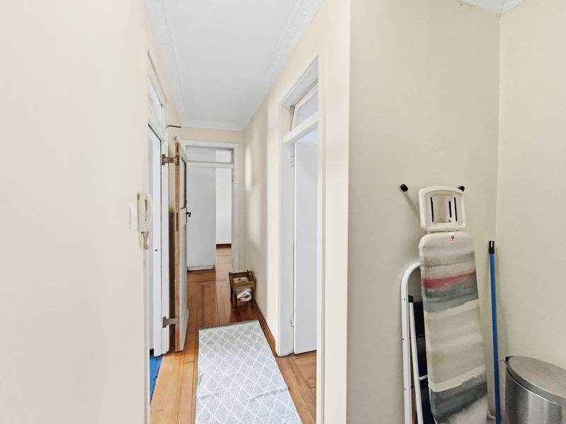 A bright, functional hallway featuring original hardwood flooring, classic cornice detailing, and multiple doorways leading to adjacent rooms.