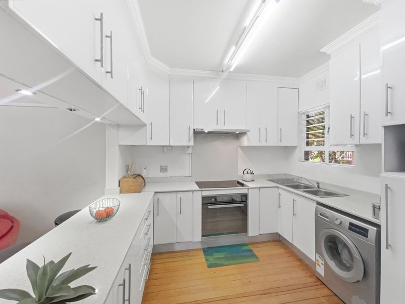Modern kitchen featuring white high-gloss cabinetry, stone countertops, integrated oven and hob, and warm hardwood flooring.