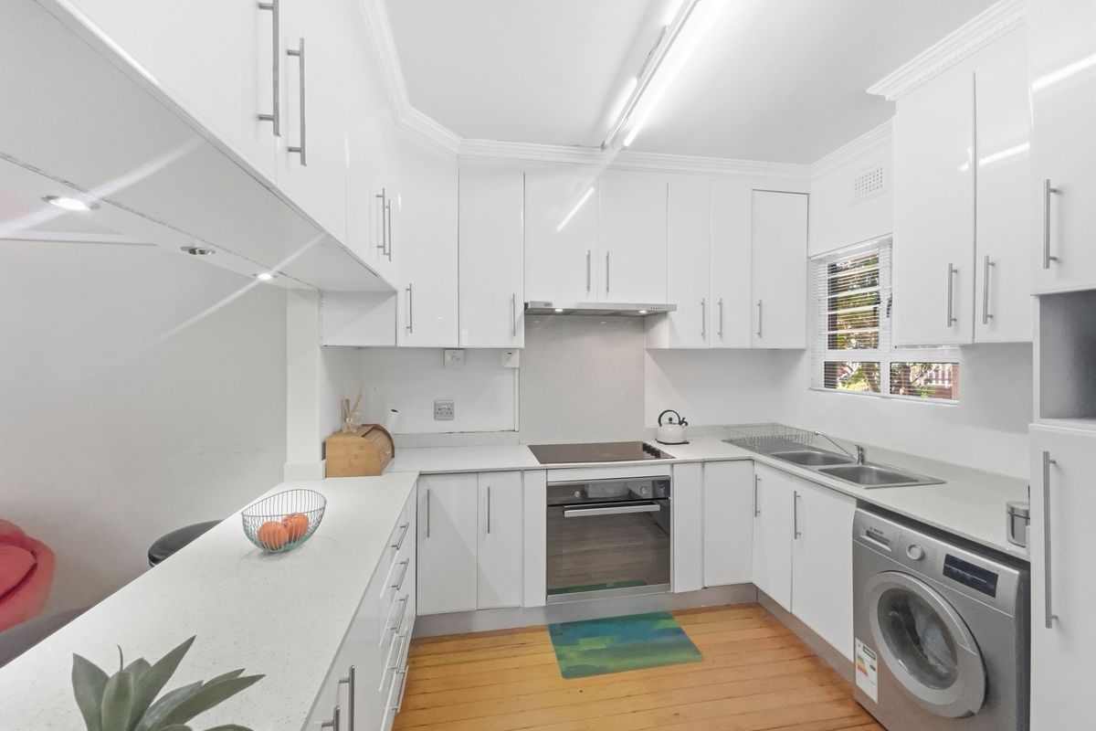 Modern kitchen featuring white high-gloss cabinetry, stone countertops, integrated oven and hob, and warm hardwood flooring.