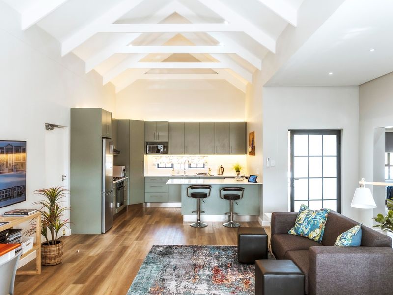 Modern open-plan living area featuring a high vaulted ceiling with exposed rafters, sleek cabinetry, and a functional kitchen island with integrated appliances.